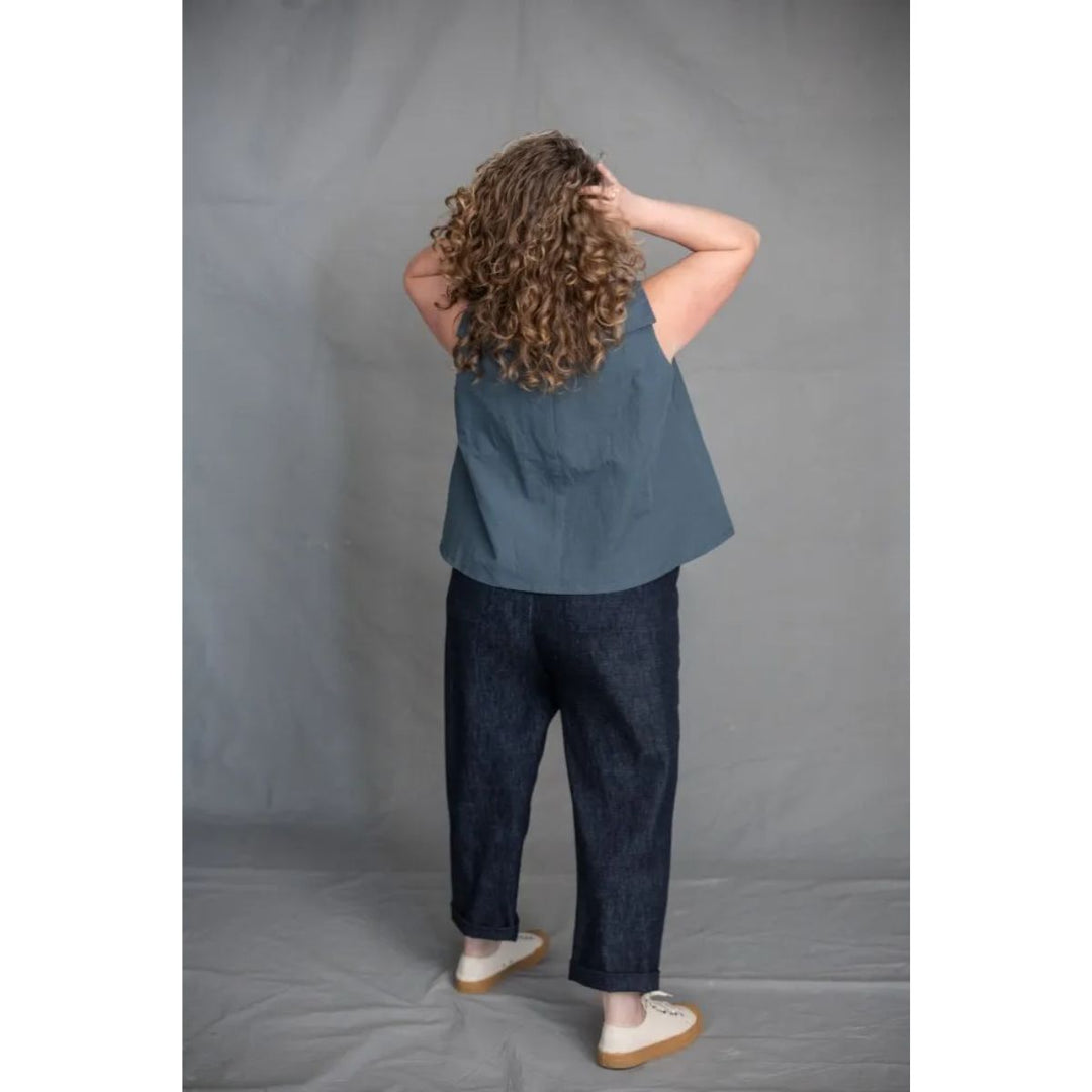 Person wearing a blue sleeveless top and dark jeans standing against a plain gray background