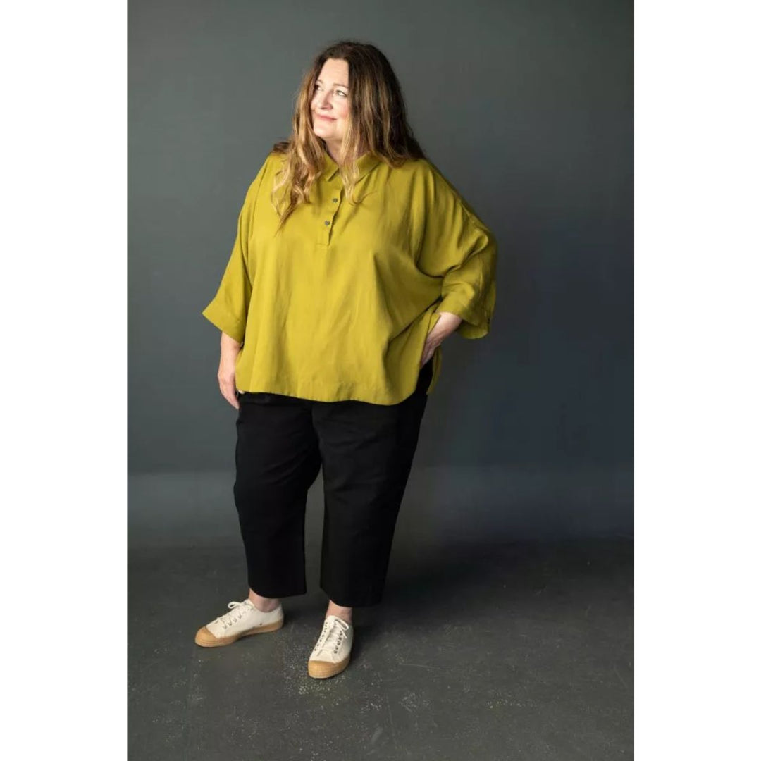 Woman wearing a mustard yellow blouse and black pants against a gray background