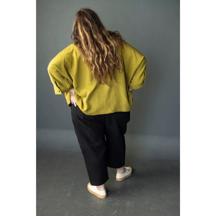 Person wearing a mustard yellow sweater and black pants against a gray background