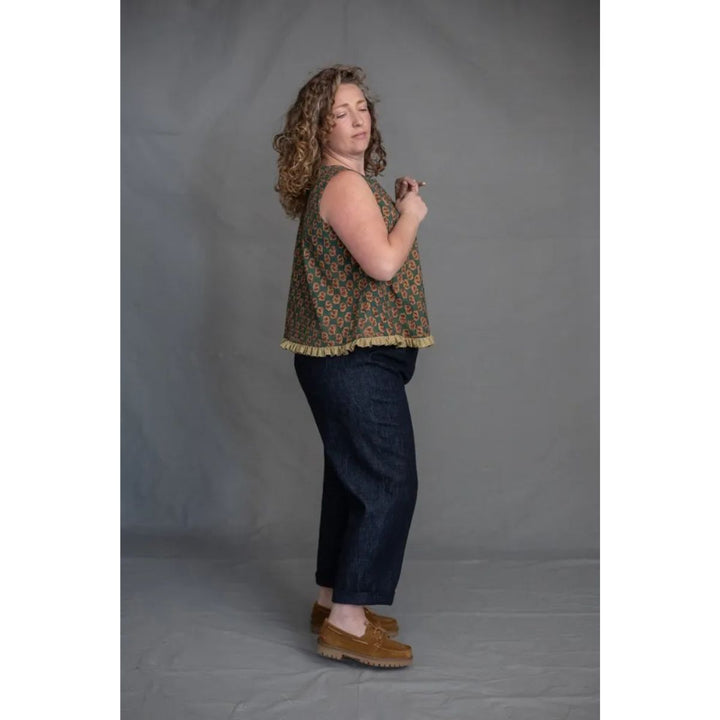 Woman wearing a patterned top and dark jeans against a plain background
