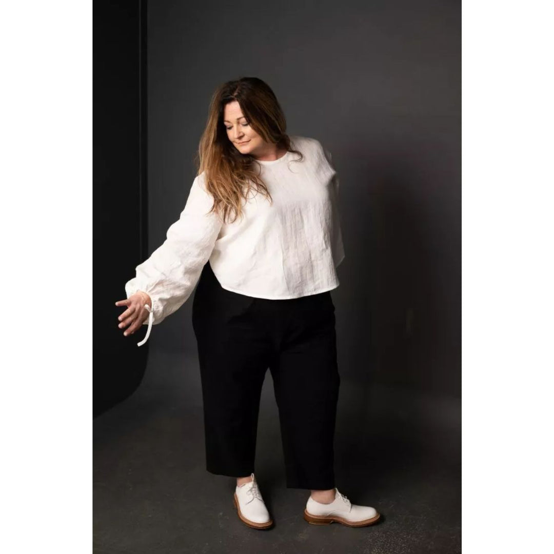 Woman wearing a white blouse and black pants against a dark background