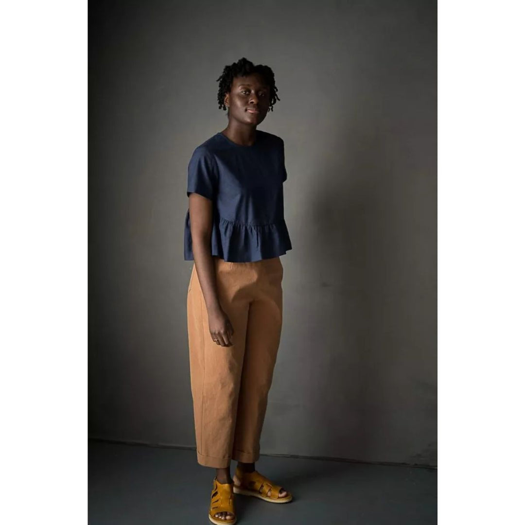 Woman wearing a blue top and brown pants against a dark background