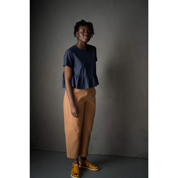 Woman wearing a blue top and brown pants against a dark background