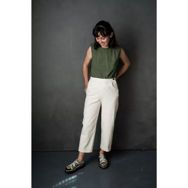 Woman wearing a green sleeveless top and white pants against a dark gray background