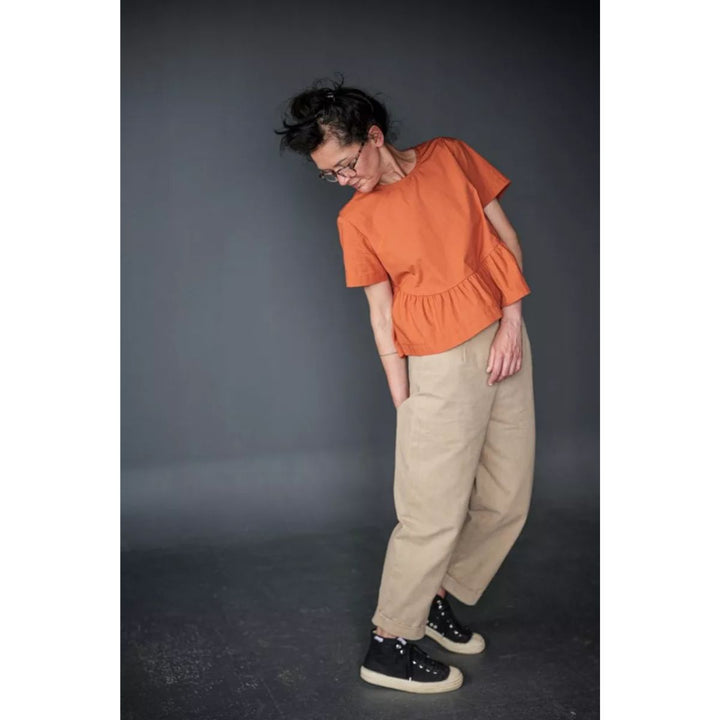 Person wearing an orange top and beige pants against a dark background