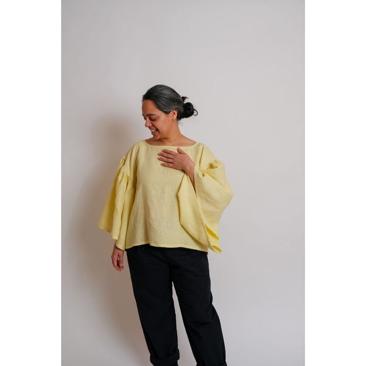 Person wearing a yellow blouse and black pants against a plain background