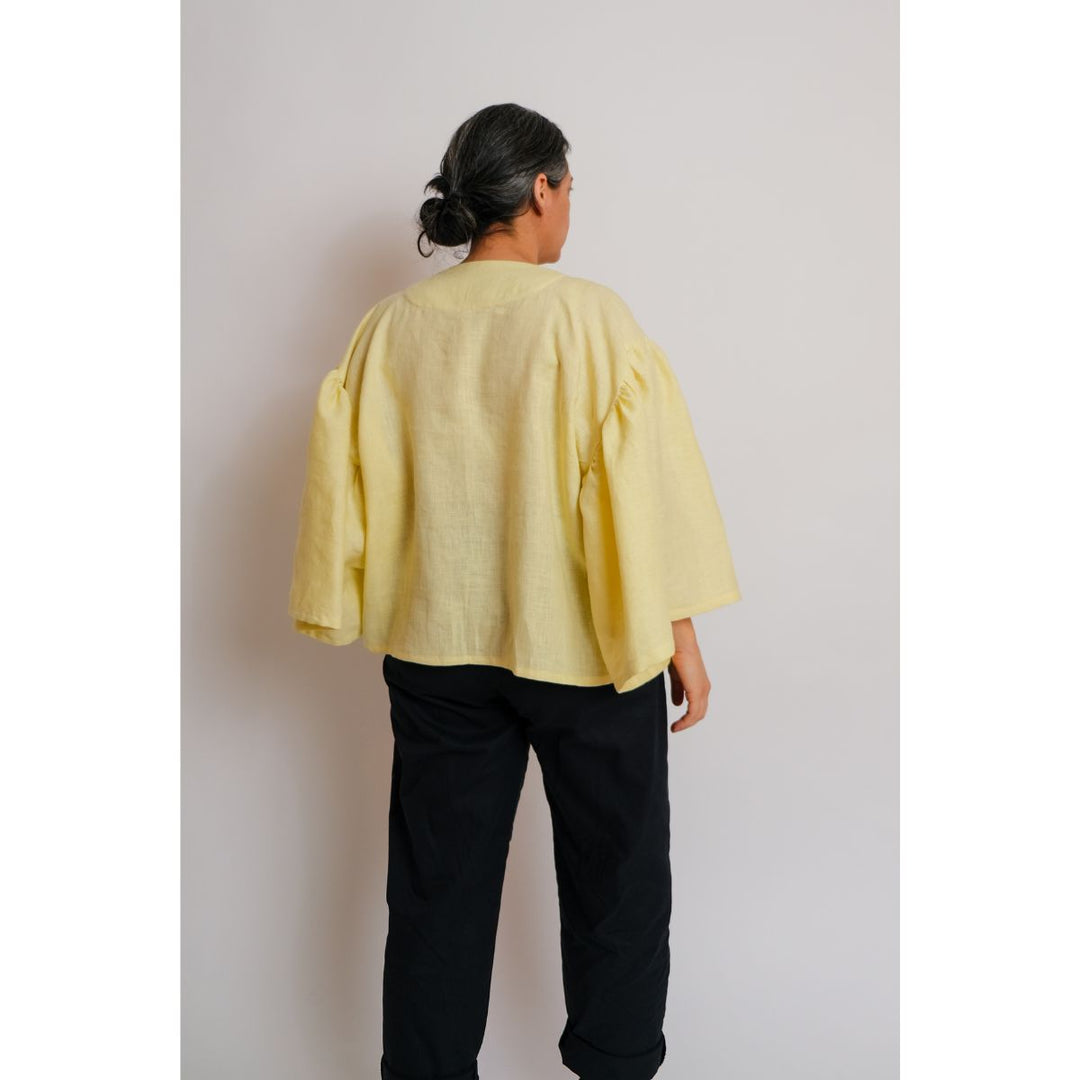 Person wearing a yellow top and black pants against a plain background