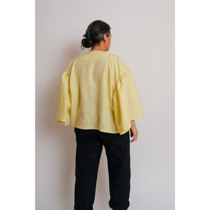 Person wearing a yellow top and black pants against a plain background