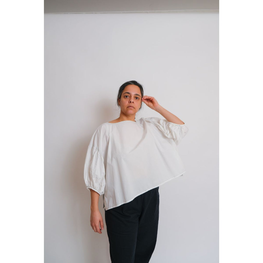 Person wearing a white blouse with puffed sleeves against a plain background