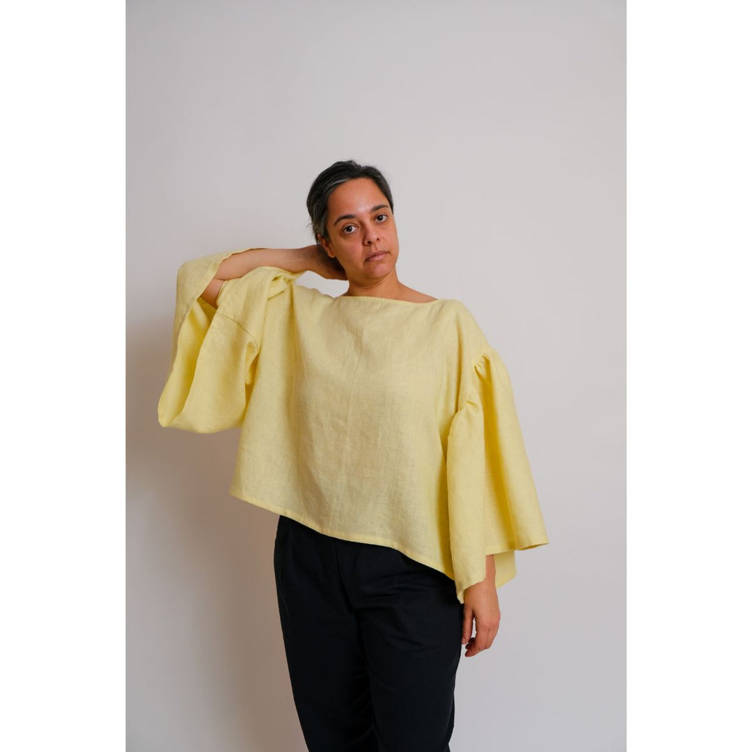 Person wearing a yellow blouse with wide sleeves against a plain background