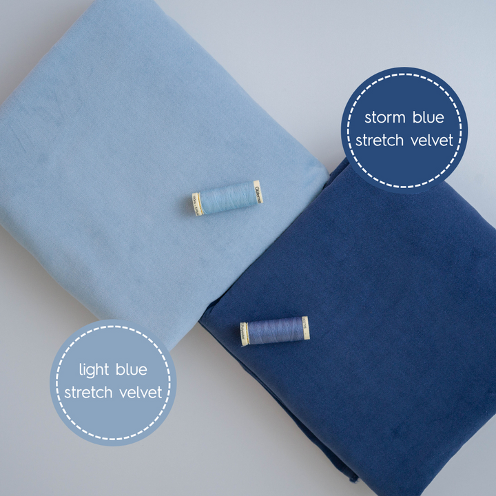 Two rolls of stretch velvet fabric, one light blue and one storm blue, on a light gray background.