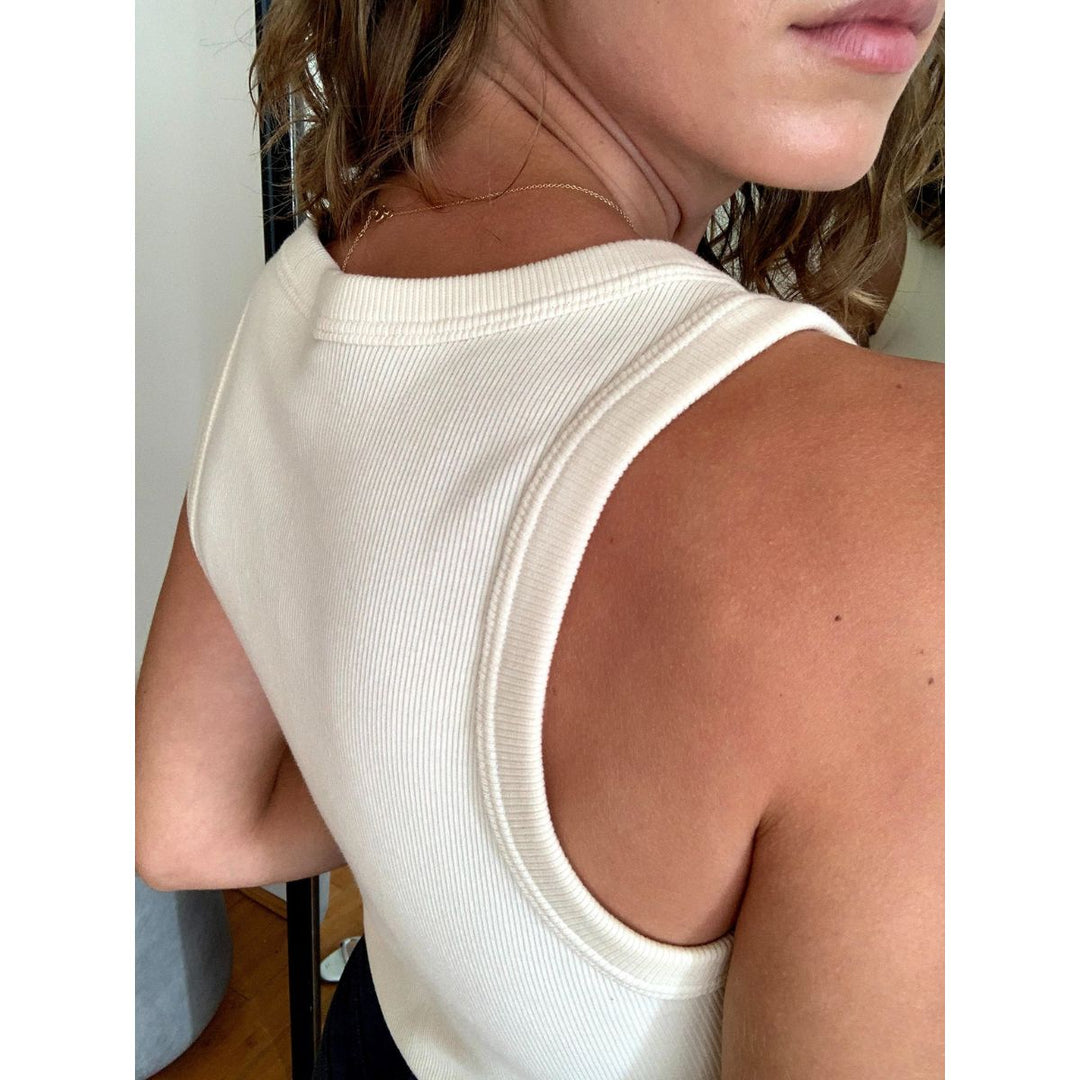 Close-up of a person wearing a white sleeveless top with a blurred background