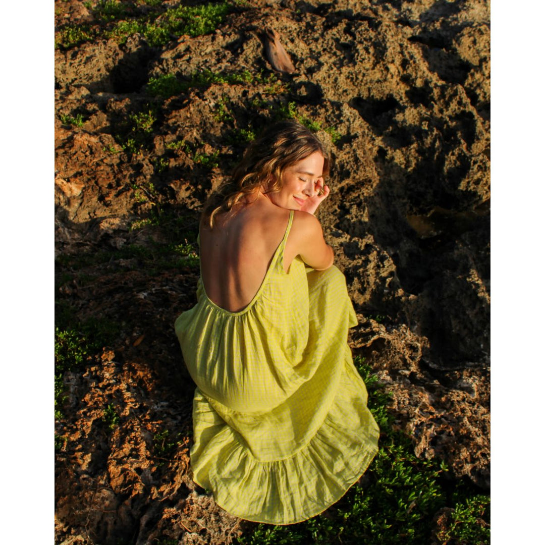Woman in a yellow dress sitting on a rocky surface with sunlight filtering through.