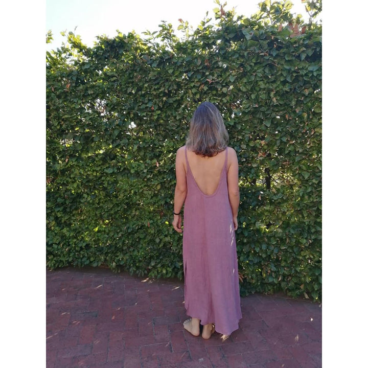 Woman in a long, light-colored dress standing in front of a green hedge.