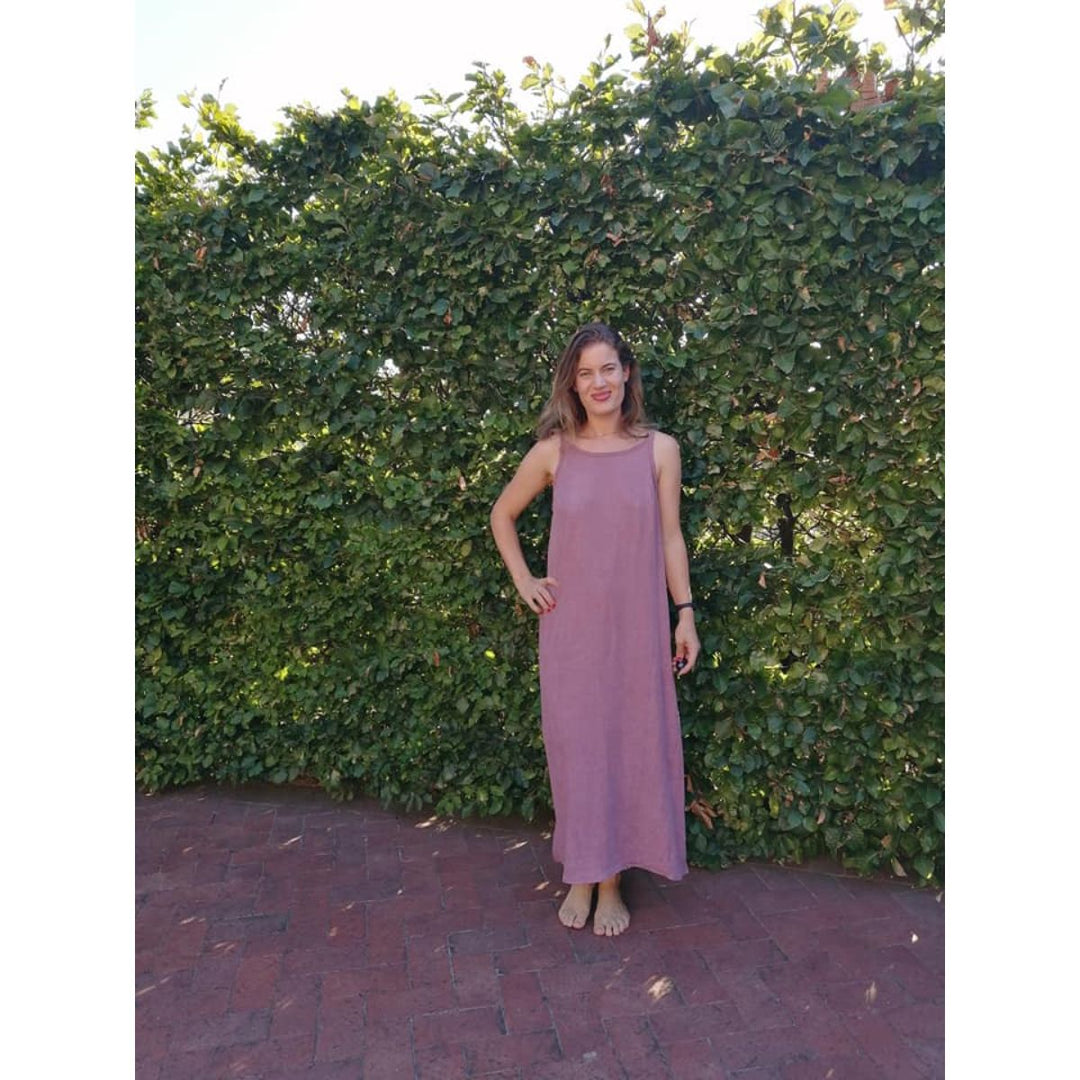 Woman in a purple dress standing in front of a green hedge.