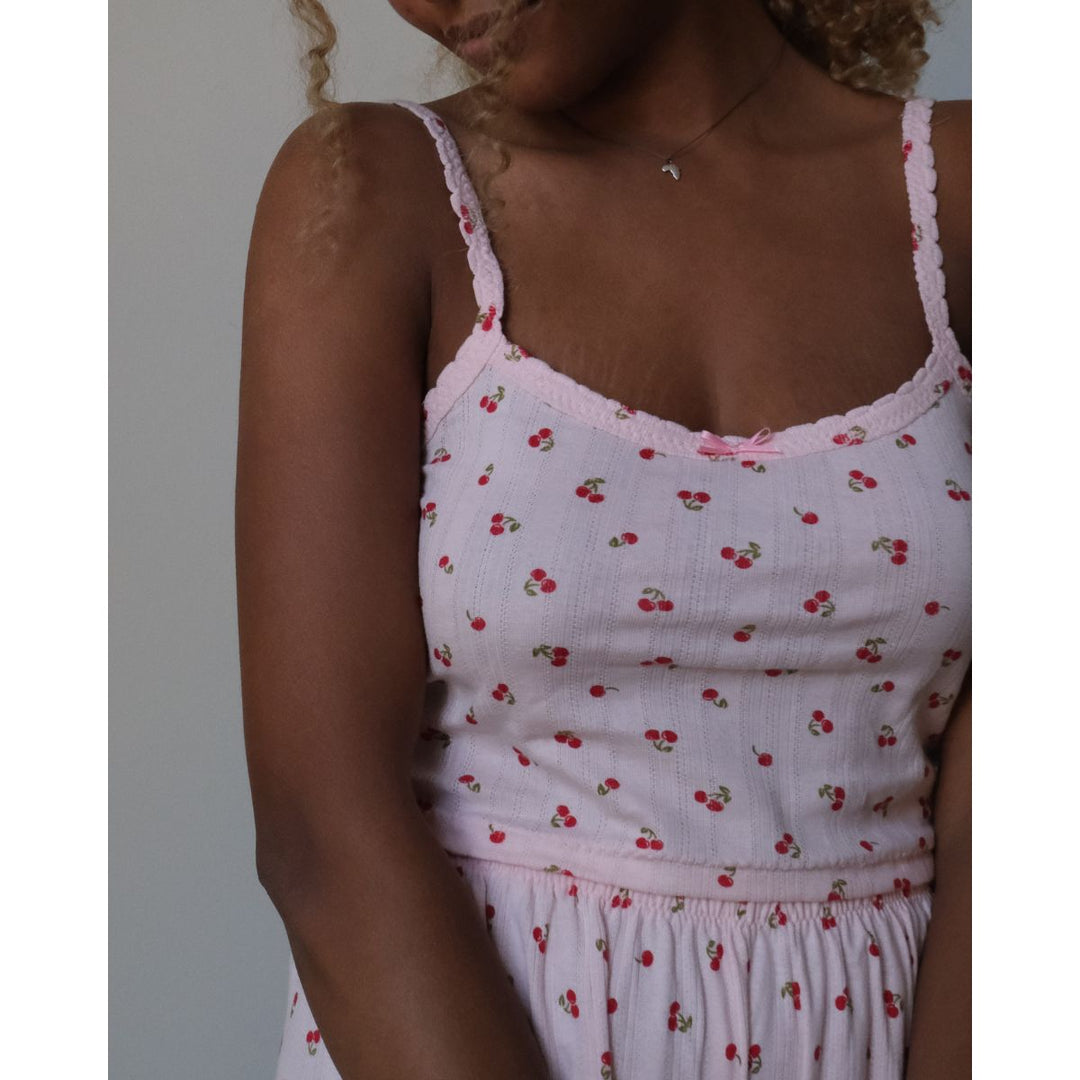 White tank top with red cherry pattern worn by a person against a neutral background