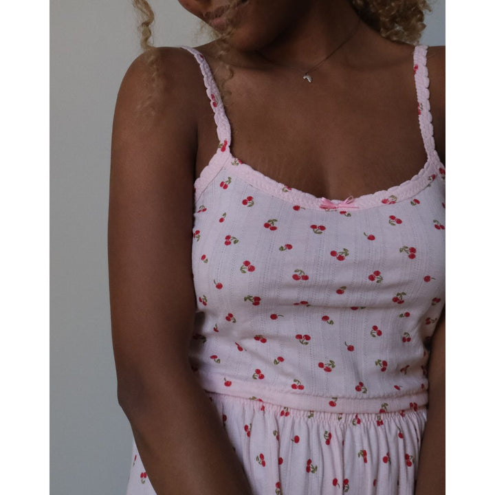 White tank top with red cherry pattern worn by a person against a neutral background