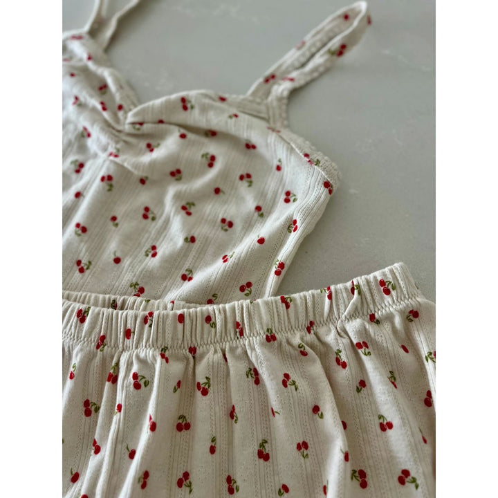 White children's dress with red cherry pattern on a light gray background