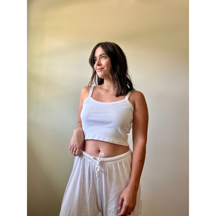 Woman wearing a white tank top and shorts against a plain background