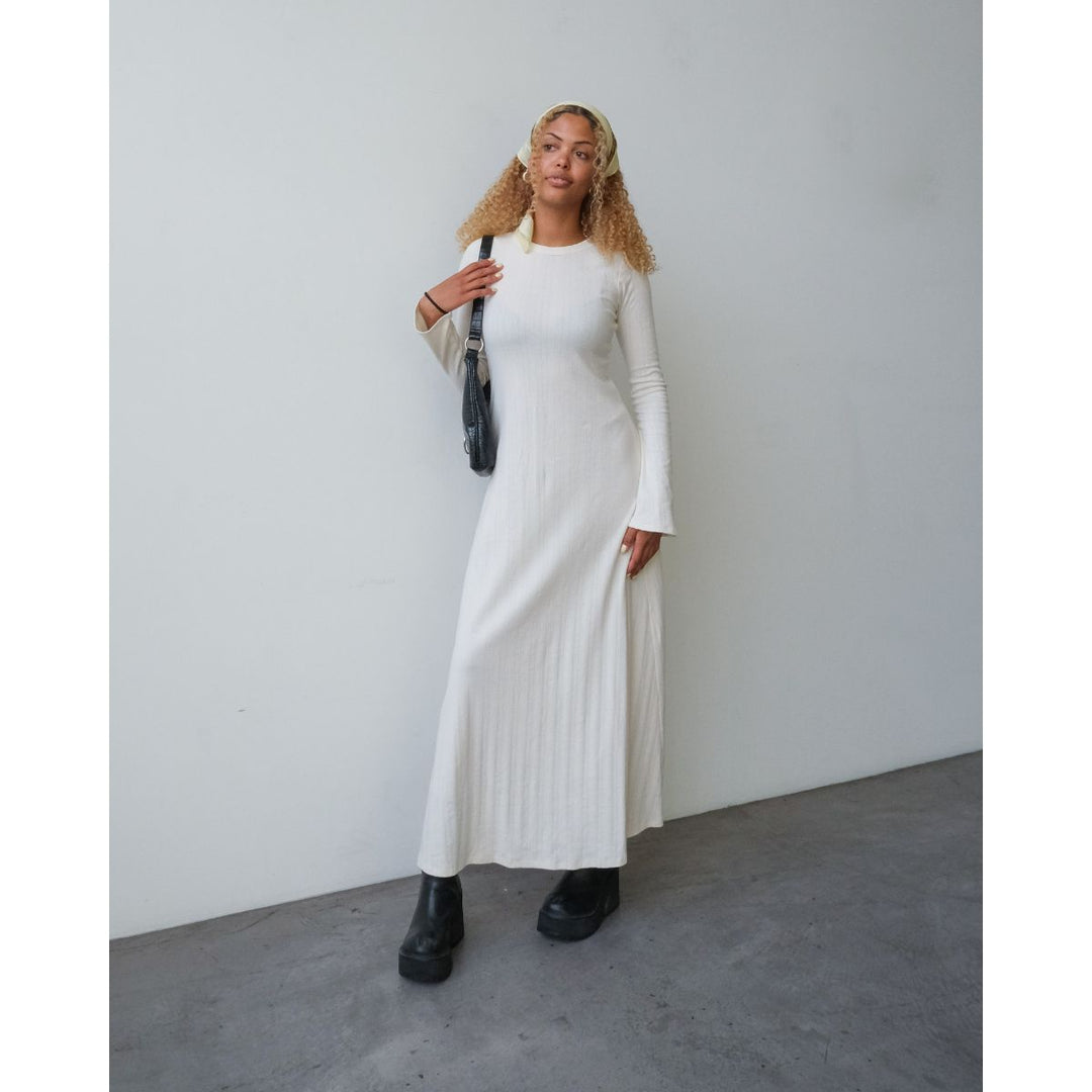Woman wearing a long white dress against a plain background