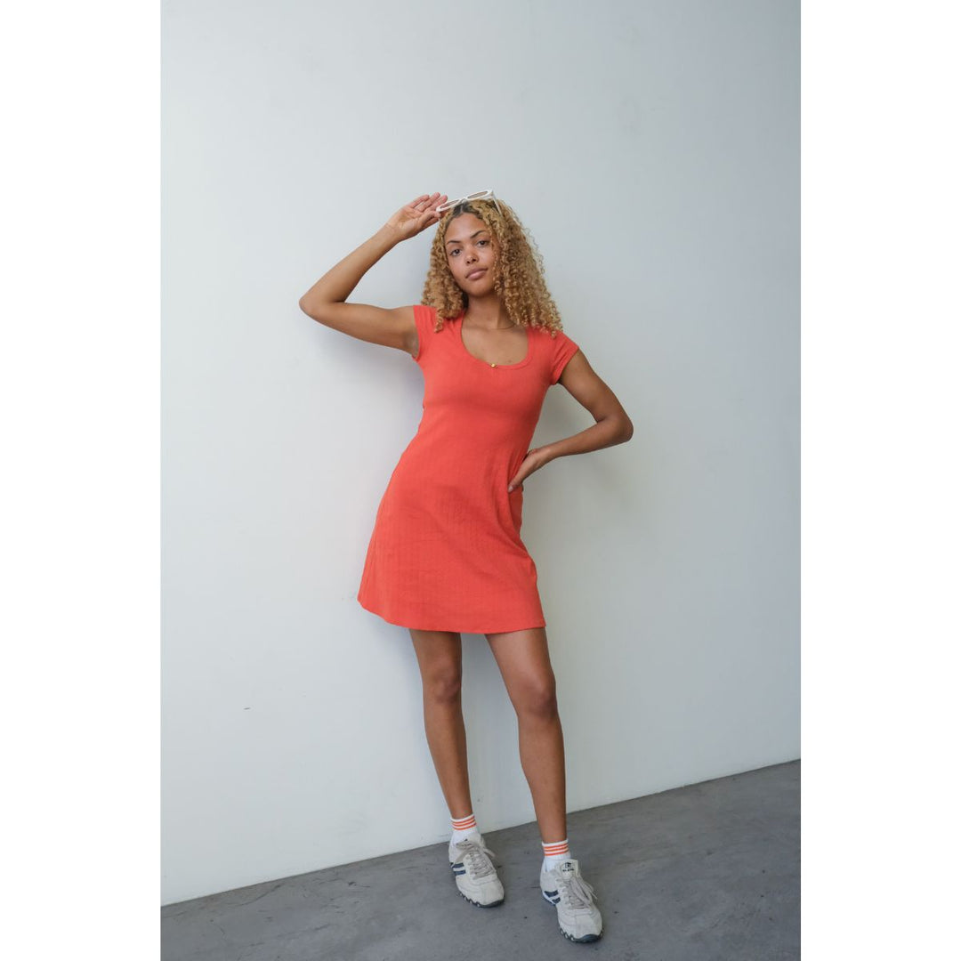 Woman wearing a red dress standing against a plain white wall.