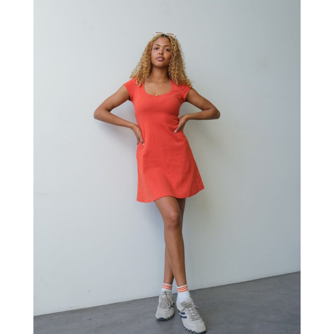 Woman wearing a red dress standing against a plain white wall.