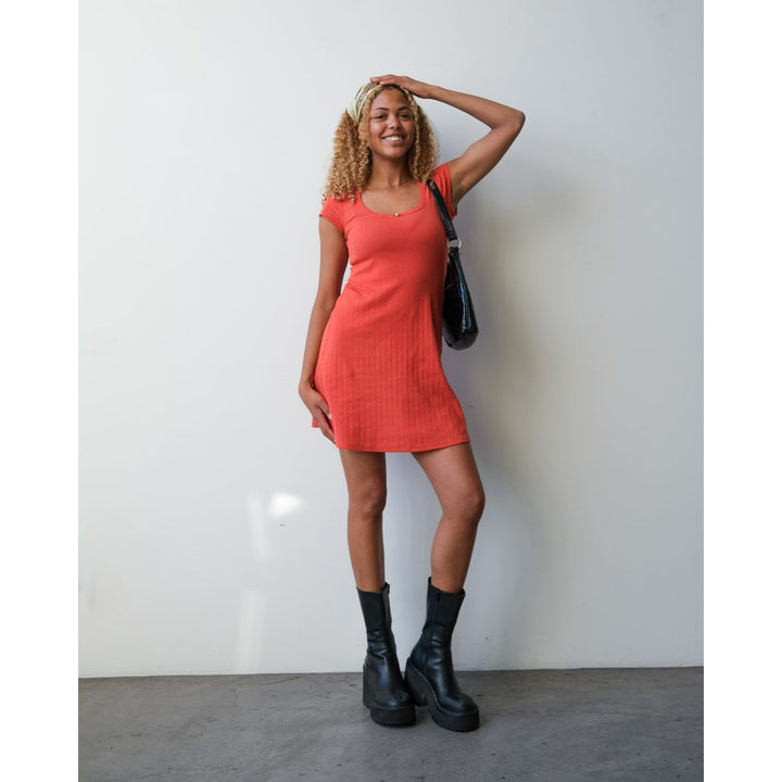 Woman in a red dress and black boots posing against a white wall.