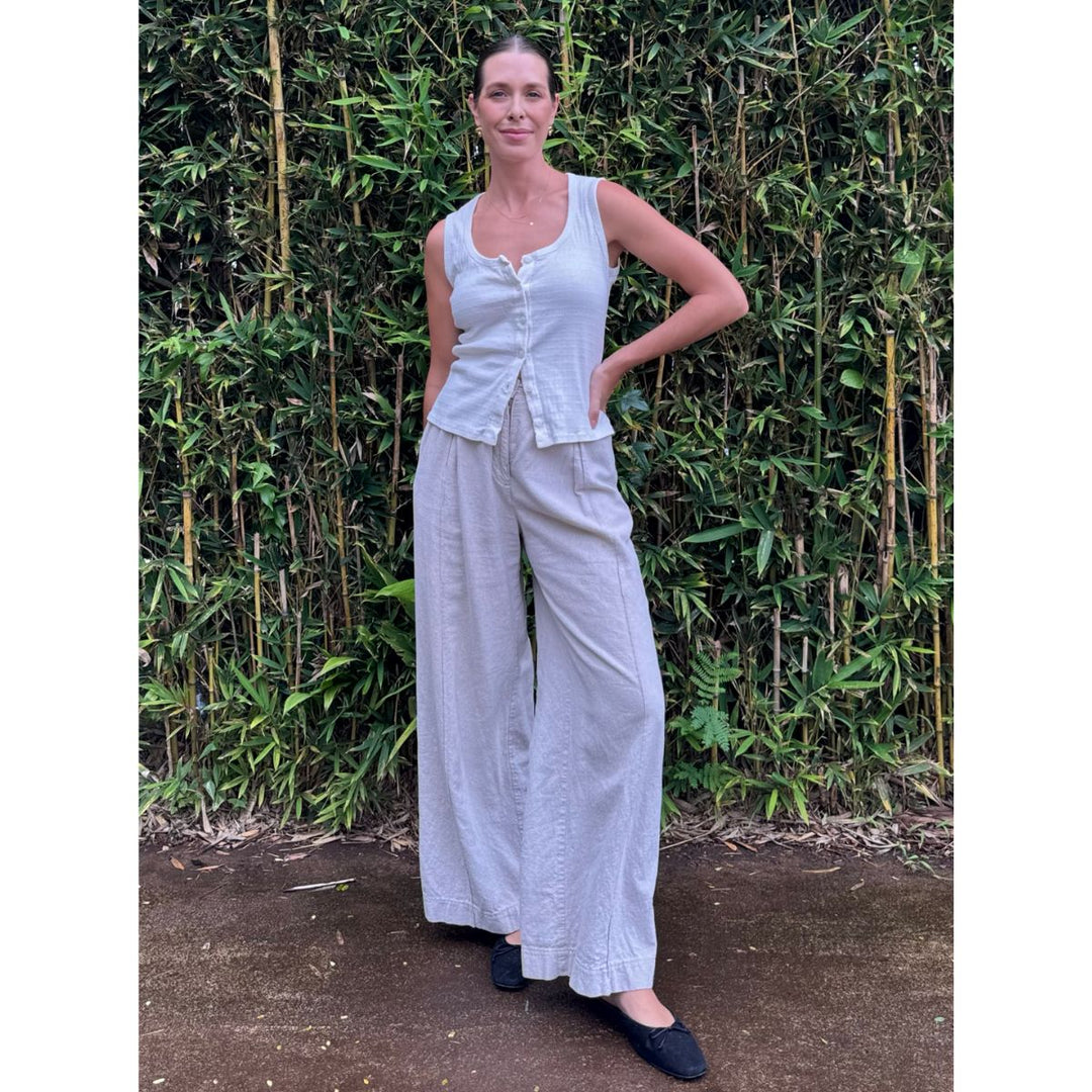 Woman in a light blue sleeveless top and wide-leg pants standing against a bamboo background