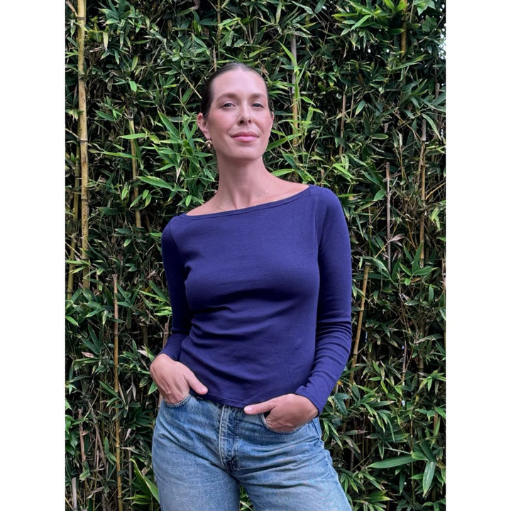 Woman wearing a blue top and jeans standing against a green leafy background