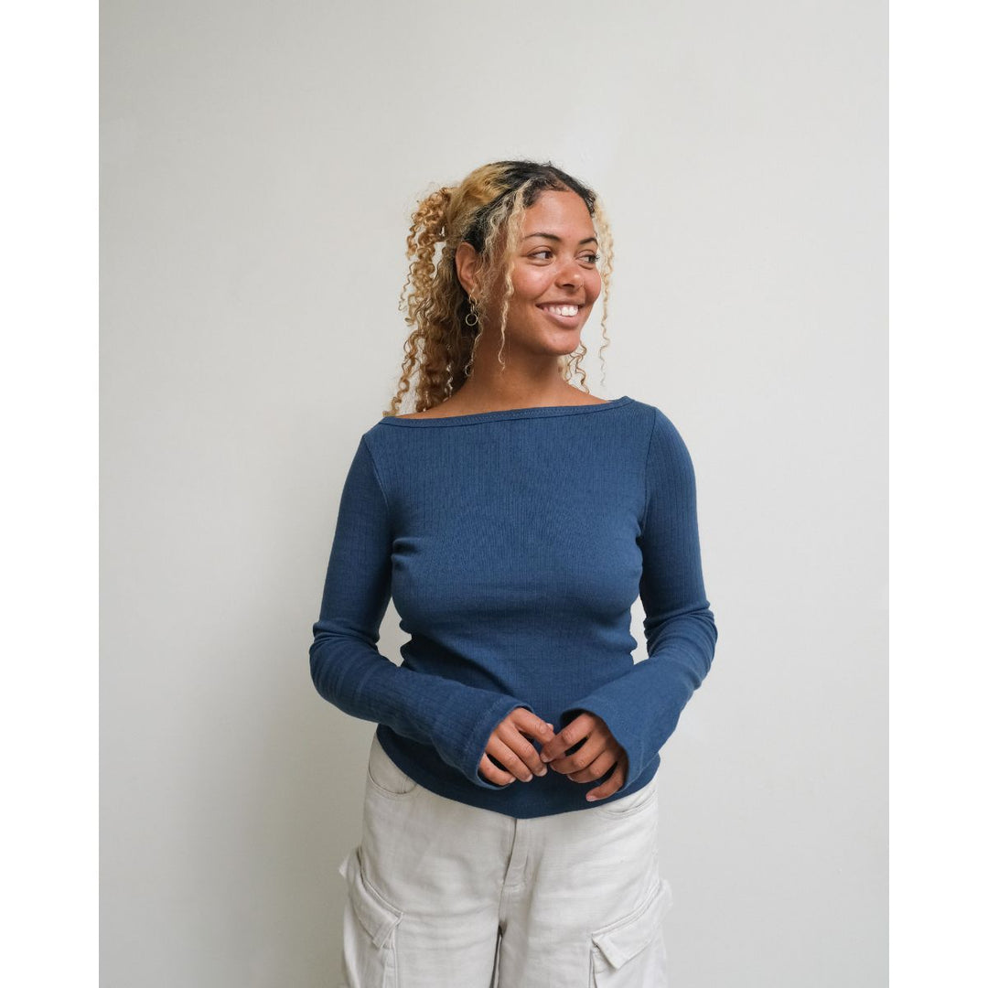 Woman wearing a blue sweater and light gray pants against a plain background