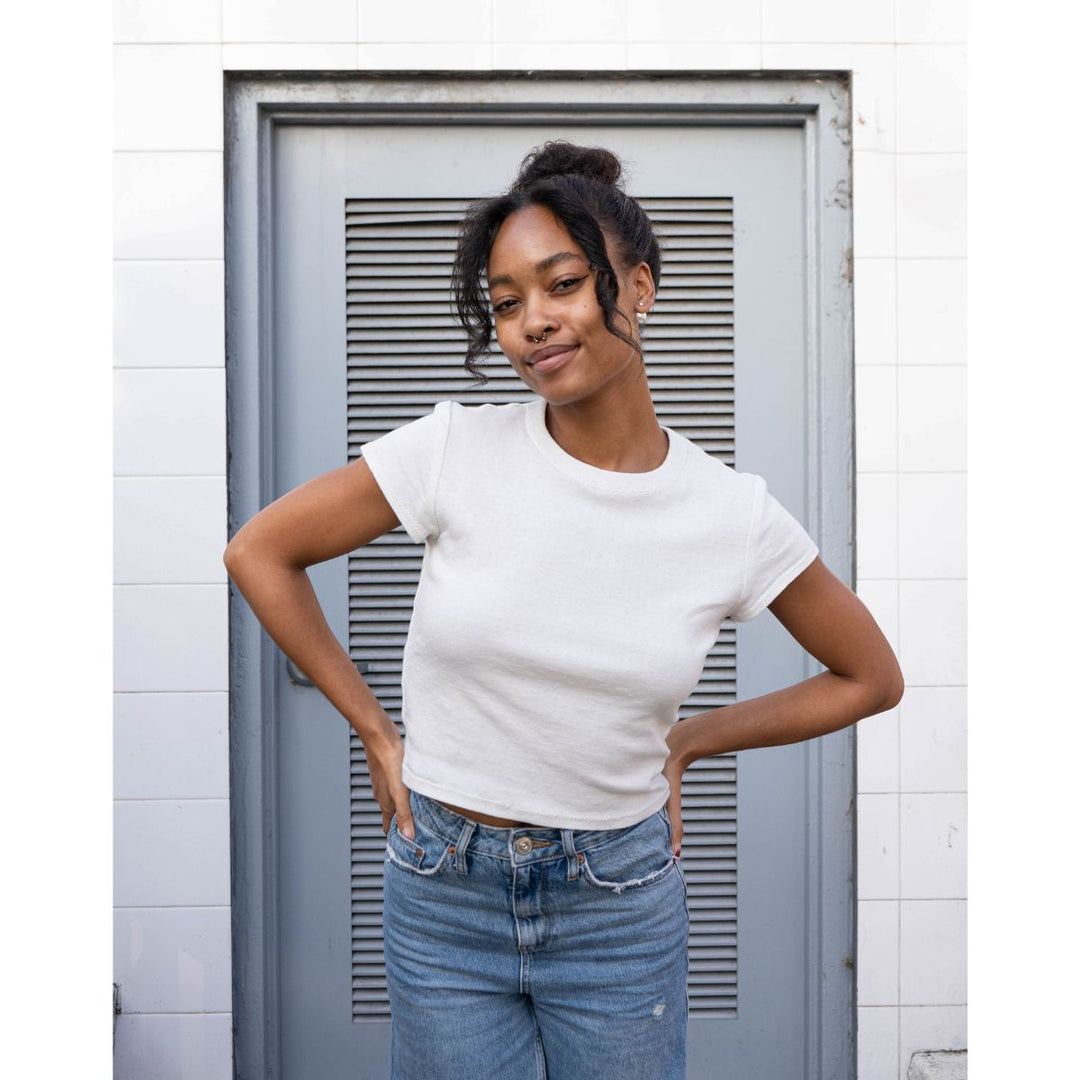 Woman wearing a white t-shirt and blue jeans standing in front of a gray door.