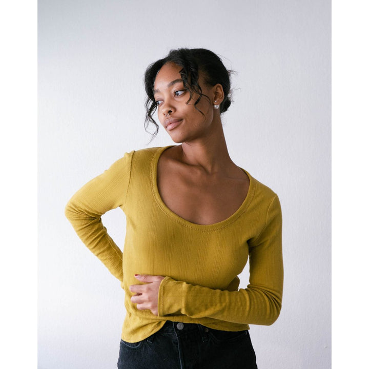 Woman wearing a mustard yellow long-sleeve top against a white background