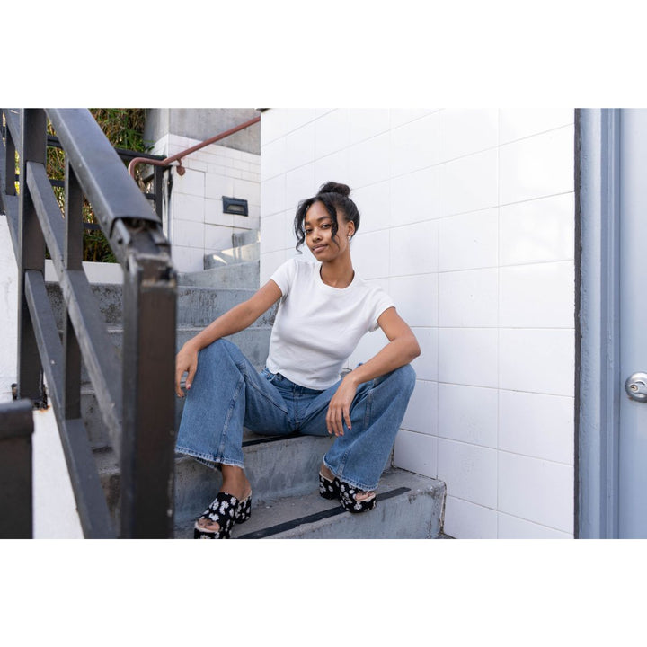 Woman sitting on a staircase wearing a white t-shirt and blue jeans.