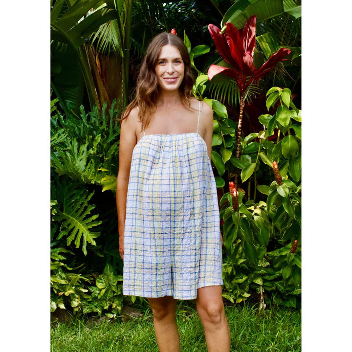 Woman wearing a checkered dress standing in a lush green garden.