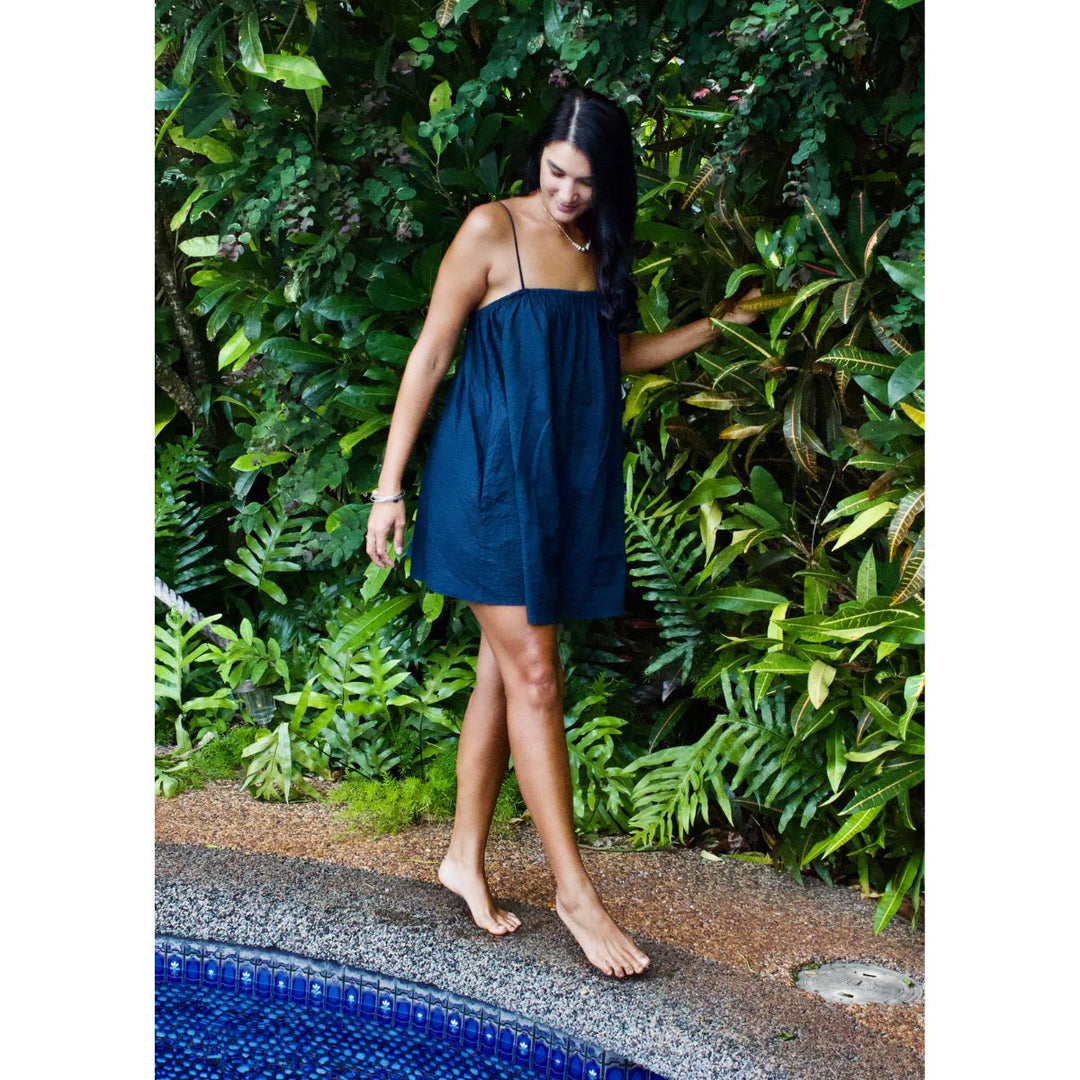 Woman in a blue dress standing by a pool with greenery in the background