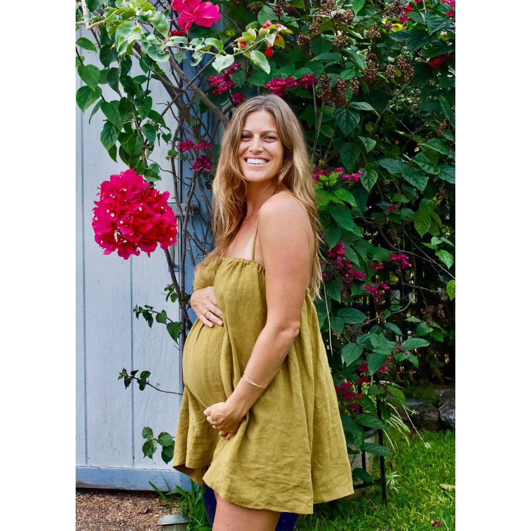 Woman in a yellow dress standing in a garden with flowers and a blue wall.