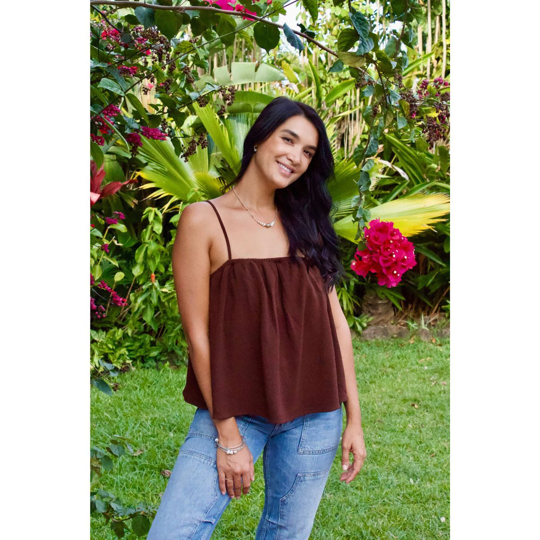 Woman wearing a brown top and blue jeans standing in a garden with greenery and flowers.