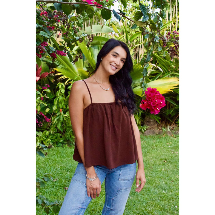 Woman wearing a brown top and blue jeans standing in a garden with greenery and flowers.