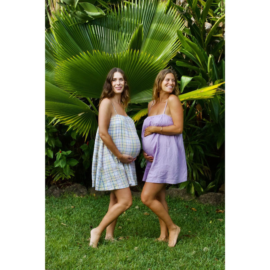 Two pregnant women standing outdoors with greenery in the background