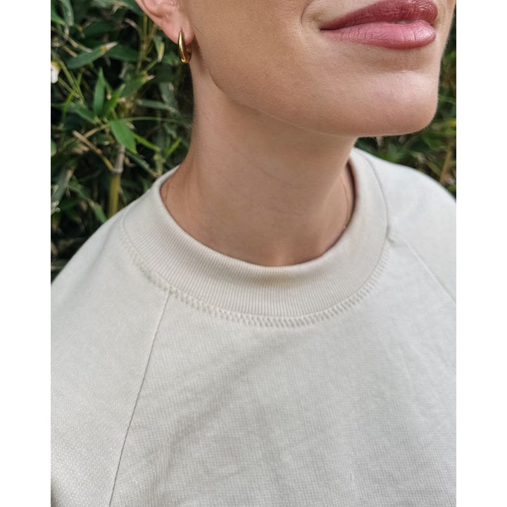 Close-up of a person wearing a light gray sweatshirt with a blurred natural background
