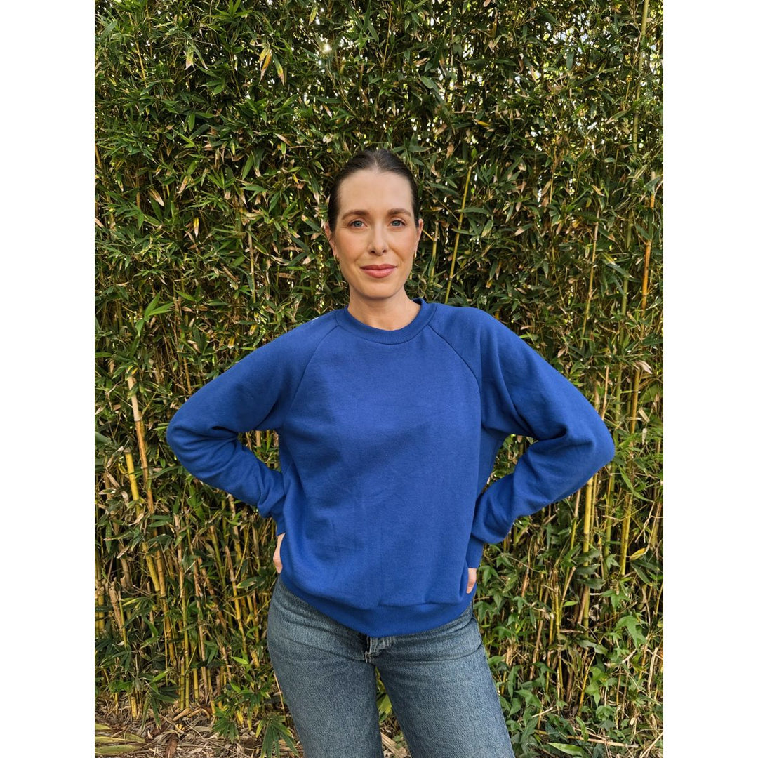 Person wearing a blue sweatshirt standing against a green bush background