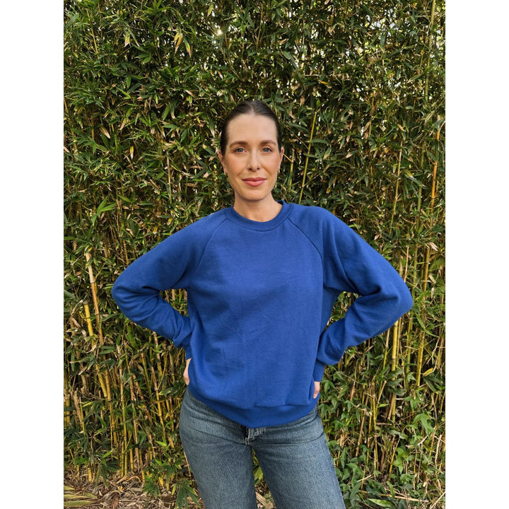 Person wearing a blue sweatshirt standing against a green bush background