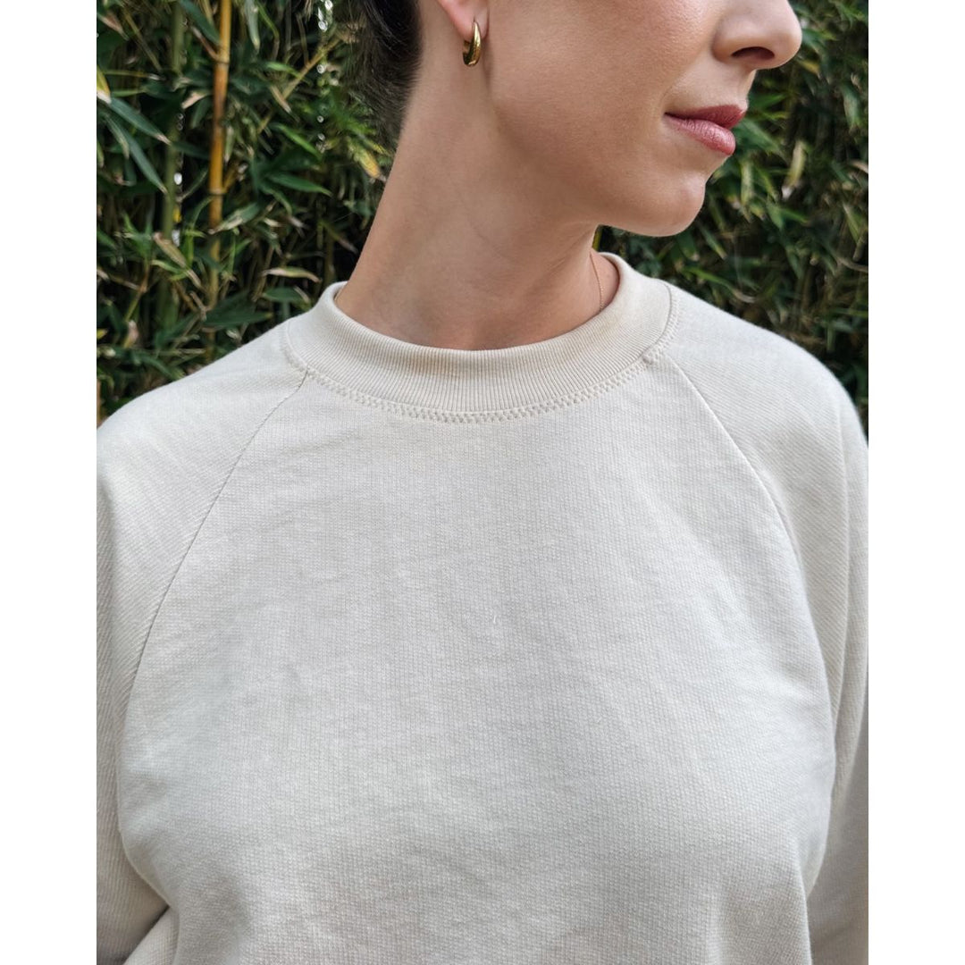 Person wearing a beige sweater with a blurred green background