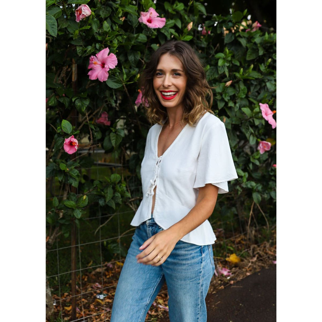 Woman wearing a white blouse and blue jeans standing in front of a floral background