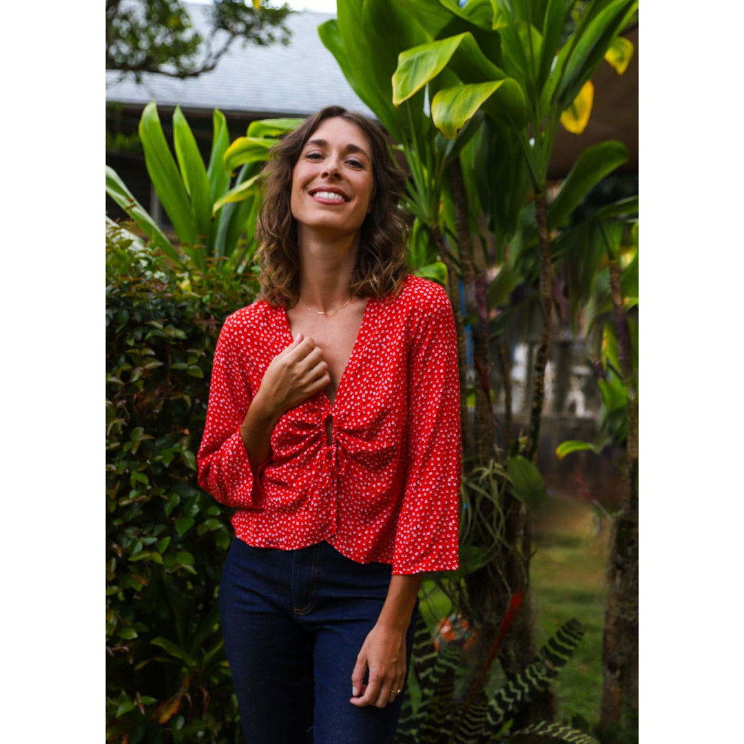 Woman wearing a red polka dot blouse standing among green plants