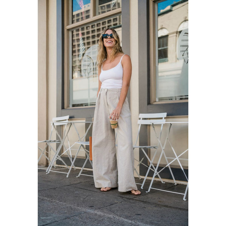 Woman in a white tank top and beige wide-leg pants standing on a city street.