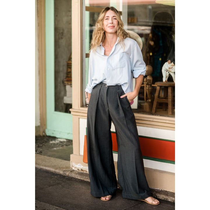 Woman standing outside a store wearing a light blue shirt and dark gray pants.