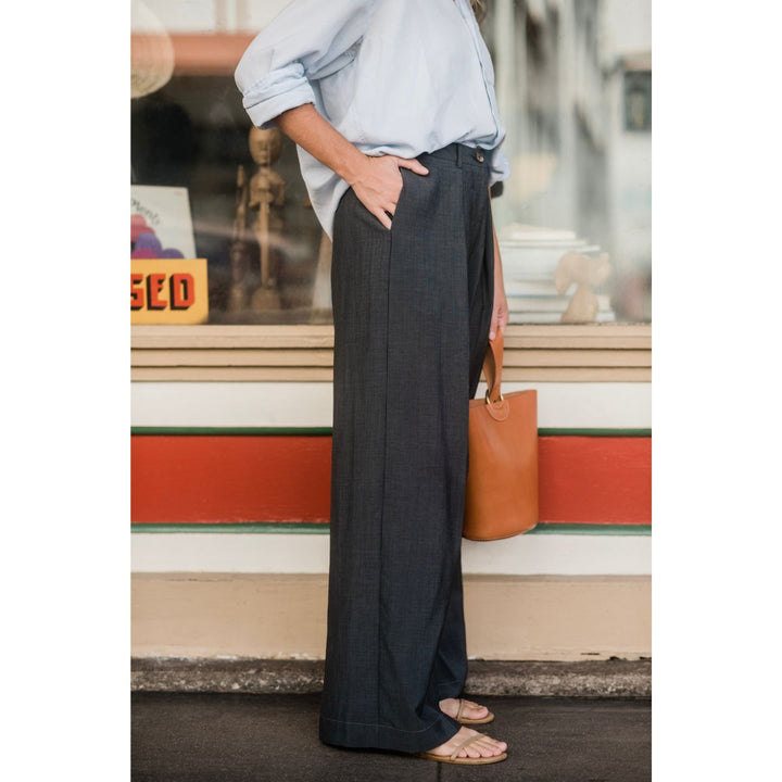 Person wearing dark wide-leg pants and a light shirt, standing in front of a store window.
