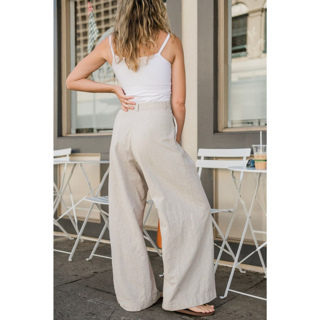 Woman wearing a white tank top and beige wide-leg pants standing outdoors.