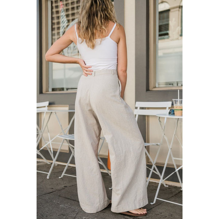 Woman wearing a white tank top and beige wide-leg pants standing outdoors.
